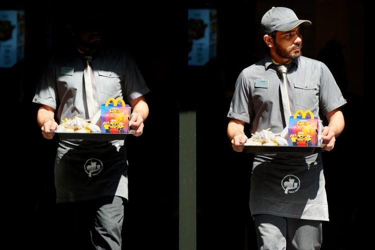 John MacLean Two and TwoMcDonald's employee in London Uk brings out Happy Meal from dark interior onto bright street. Photograph by artist john MacLean grey uniform