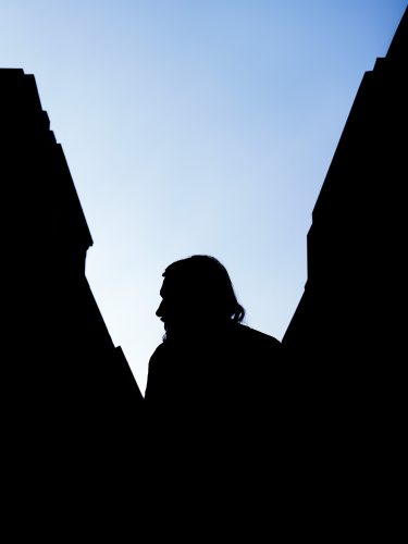 John MacLean A to Bsilhouette of man with beard between two dark buildings London Uk