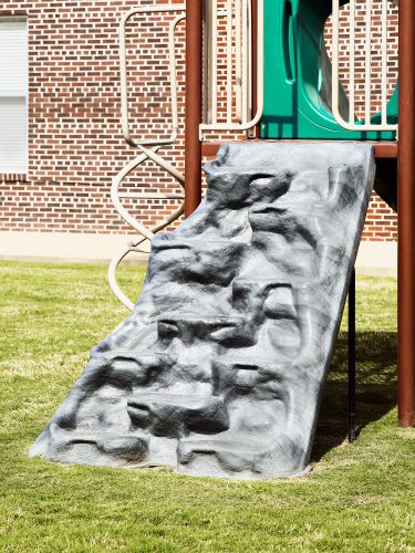 John MacLean CityChildren's playground. climbing frame with green grass and red brick wall. Art photograph by John MacLean London Uk based artist.