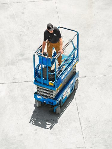 John MacLean Cityelderly man driving blue scissor lift yellow trousers