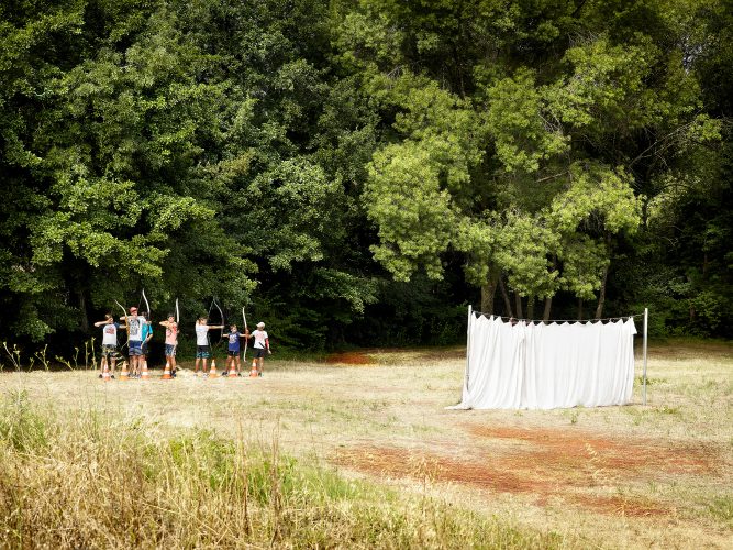 John MacLean Your NatureA group of young men in casual summer clothes practice archery in an open field near Lac du Salagou, South France. The scene deliberately withholds the identity of the target, leaving the viewer to contemplate its nature. A white sheet hung on poles in the foreground obscures part of the field, adding an air of mystery. The image evokes the themes of William Golding’s Lord of the Flies, serving as a metaphor for the latent potential of human beings for malevolence or violence. Timeless in its composition, it harks back to early human hunters from 300,000 years ago, blending modernity with primal undertones.