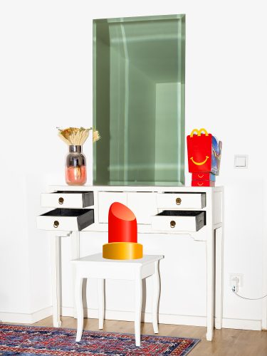 John MacLean ConversationsAn emoji of a lipstick is superimposed onto a domestic interior featuring a chair, desk, and mirror. The lipstick is placed on a stool, while on the desk, a red McDonald’s Happy Meal box with a yellow smiling logo appears to be having a conversation with the lipstick, blending surreal humour with everyday objects